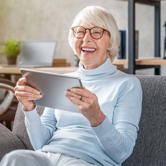 Older woman with dental implants in Brick Township laughing with tablet